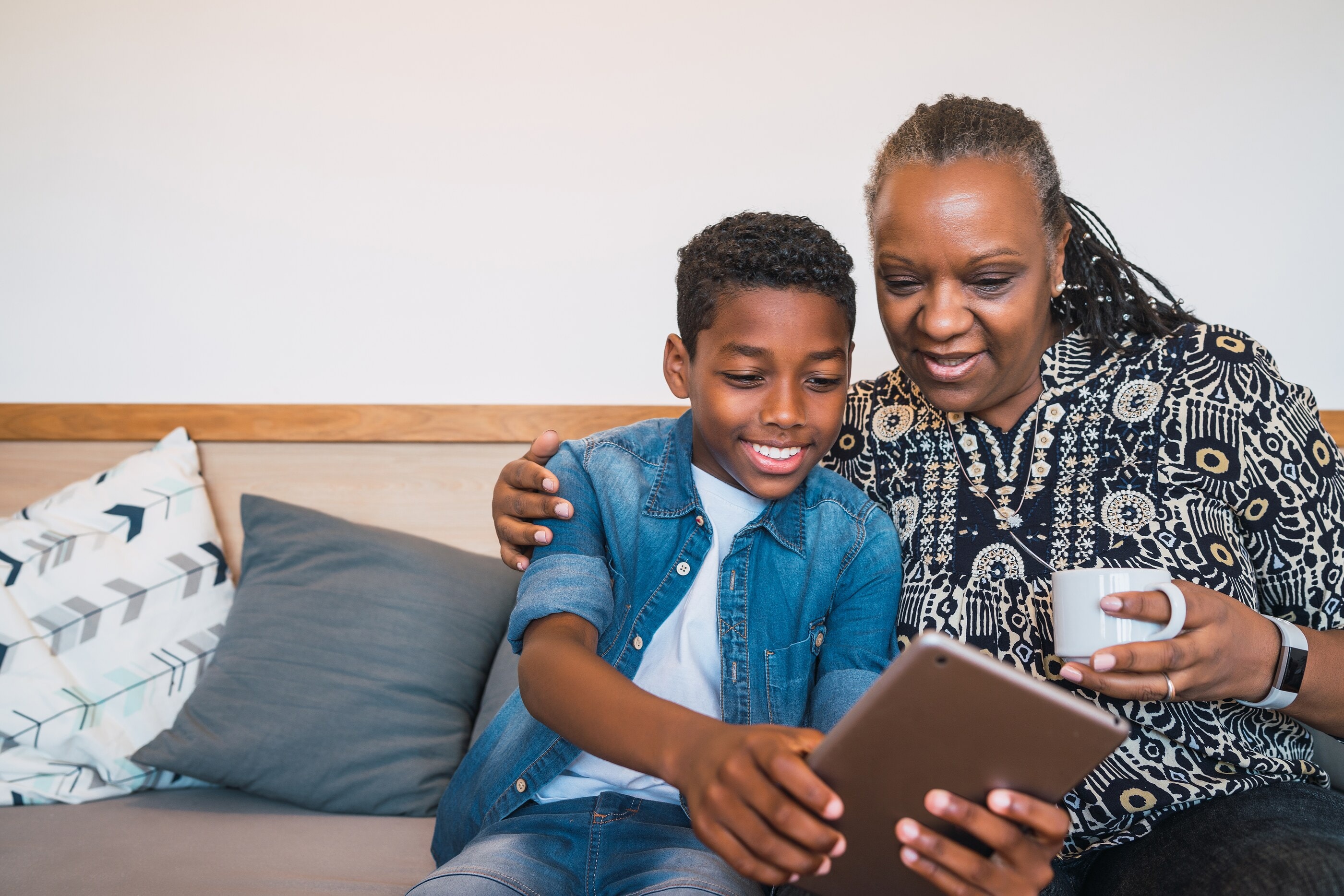 A grandmother and her grandson smiling at a tablet on the sofa
